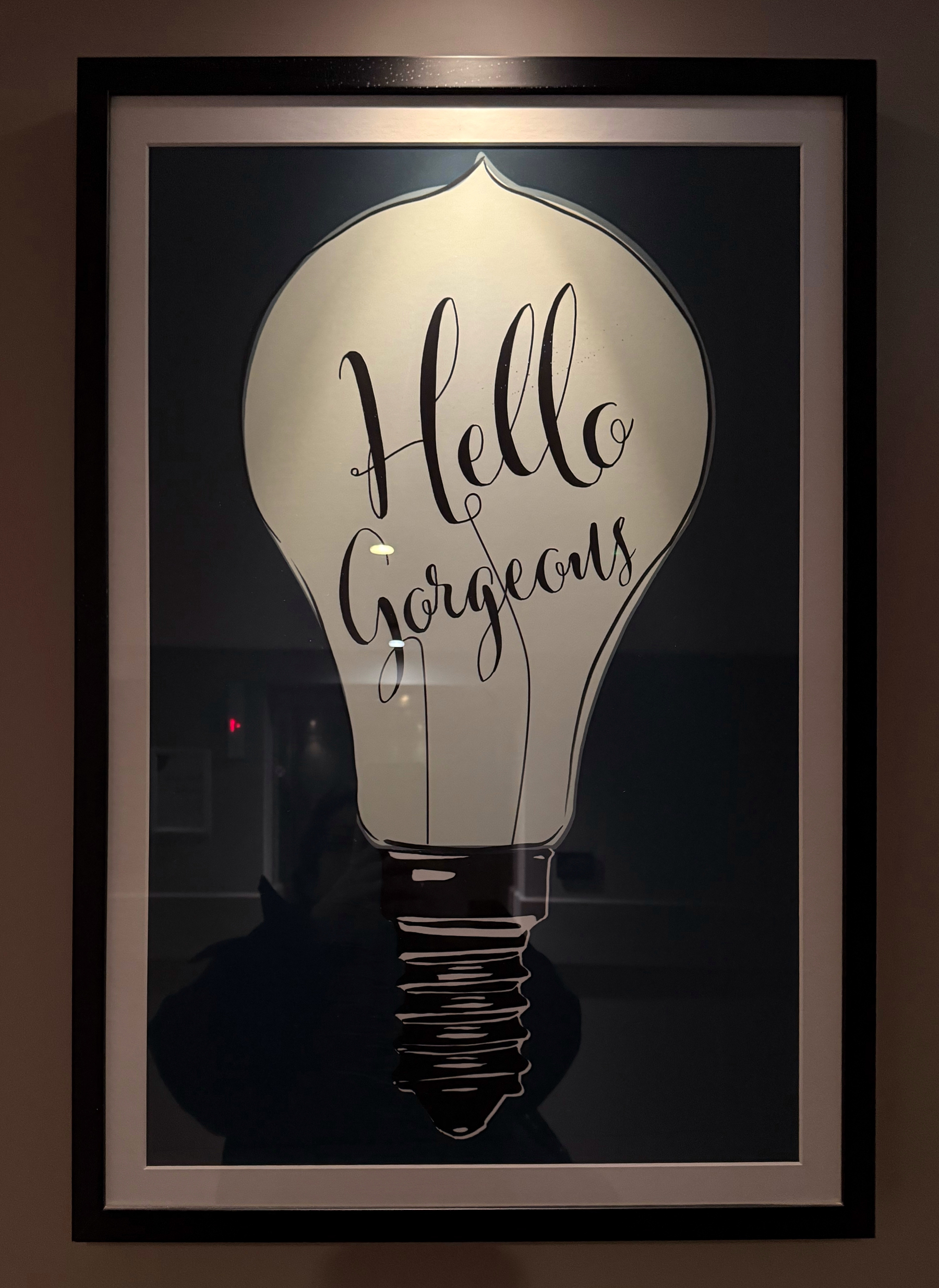 A framed artwork features a lit light bulb with the words Hello Gorgeous inside it.